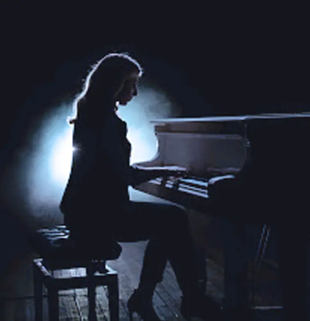 Silhouette of a person playing a grand piano on a dimly lit stage, with a bright light creating a halo effect from behind. The scene conveys a sense of drama and focus on the musician.